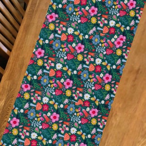 May include: A green table runner with a floral pattern featuring pink, red, yellow, blue, and white flowers, butterflies, and mushrooms.