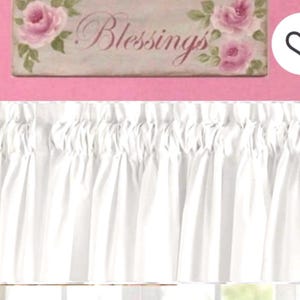 May include: White ruffled curtain valance with a pink background. Above the curtain is a rectangular sign with the word "Blessings" and pink roses painted on it.