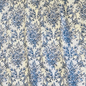 May include: White fabric with a blue floral and scroll pattern. The design features clusters of flowers and ornate scrollwork in varying shades of blue against a white background. The fabric is likely used for home decor.