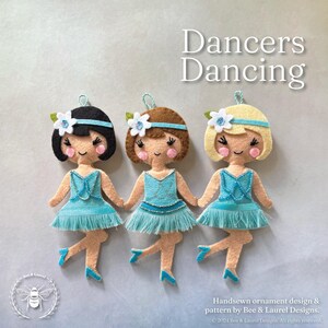 May include: Three felt ornaments of dancers in blue tutus with white flowers in their hair. The dancers are in various poses, with their arms outstretched and their legs in the air. The ornaments are hand-sewn and have a whimsical, vintage feel. The text "Dancers Dancing" is at the top of the image.
