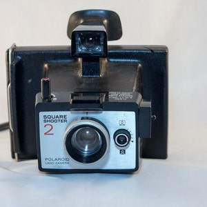 May include: A black Polaroid Square Shooter 2 Land Camera with a silver lens and a red number "2" on the front.