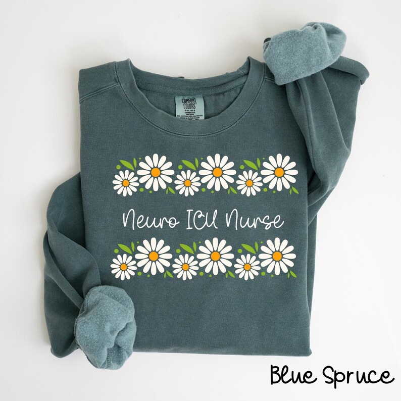 Pode incluir: Uma camisa de frio azul com uma borda de margaridas brancas e o texto "Neuro ICU Nurse".