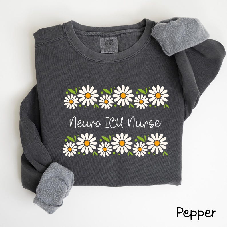 Pode incluir: Uma camisa de moletom cinza escuro com uma borda de margaridas brancas e o texto "Neuro ICU Nurse" em branco. A camisa de moletom tem um forro de l&atilde; cinza.