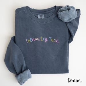 May include: A dark blue sweatshirt with the text "Telemetry Tech" embroidered in colorful letters. The sweatshirt is made of a soft, comfortable fabric and has a relaxed fit.