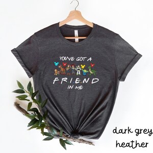 May include: Dark heather grey t-shirt with a graphic of cartoon characters from Disney and Pixar. The text on the shirt reads "You've got a friend in me".