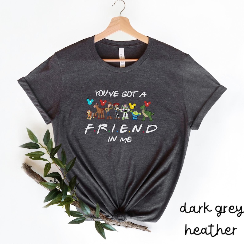 May include: Dark heather grey t-shirt with a graphic of cartoon characters from Disney and Pixar. The text on the shirt reads "You've got a friend in me".