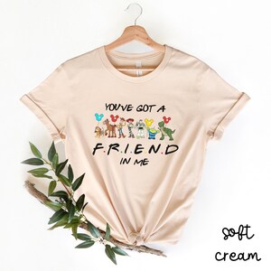 May include: A soft cream colored t-shirt with a graphic of Toy Story characters and the text "You've got a friend in me".