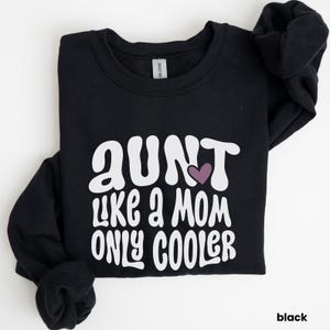 Peut inclure: Sweat-shirt noir avec un texte blanc qui dit "Tante comme une maman, mais en plus cool" avec un cœur violet.