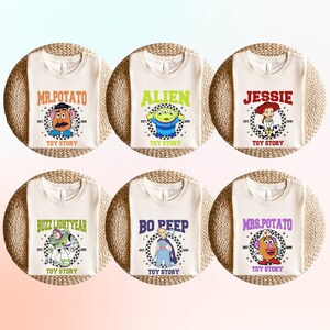 May include: Six off-white t-shirts featuring Toy Story characters: Mr. Potato Head, Alien, Jessie, Buzz Lightyear, Bo Peep, and Mrs. Potato Head. Each shirt has the character's name in a bold font, the Toy Story logo, and the year 1999.