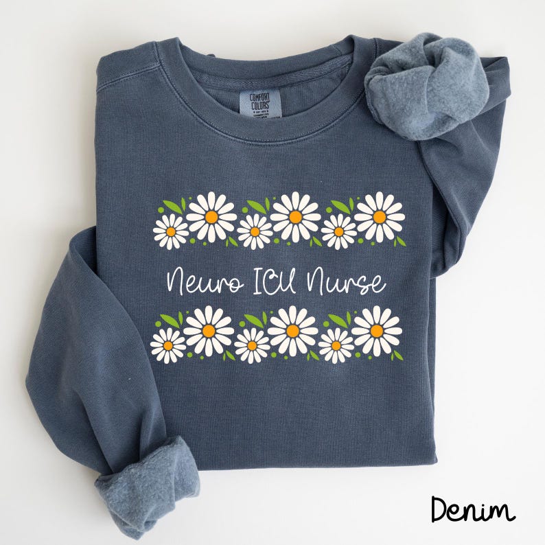 Pode incluir: Uma camisa de frio azul escura com uma borda de margaridas brancas e o texto "Neuro ICU Nurse" em branco. A camisa de frio &eacute; feita de um material macio e confort&aacute;vel.