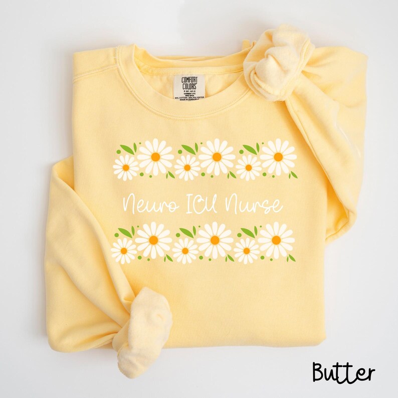 Pode incluir: Uma camisa de moletom amarela com uma borda de margaridas e o texto "Neuro ICU Nurse" impresso na frente. A camisa de moletom &eacute; feita de um material macio e confort&aacute;vel e &eacute; perfeita para o uso di&aacute;rio.