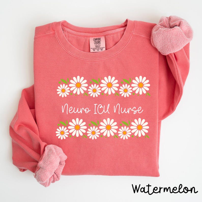 Pode incluir: Uma camisola rosa com o texto "Neuro ICU Nurse" e uma borda de margaridas brancas com folhas verdes. A camisola est&aacute; dobrada e a cor &eacute; descrita como "Watermelon".
