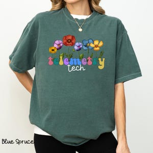 Könnte beinhalten: Ein blaugrünes T-Shirt mit einem Aufdruck von bunten Blumen und dem Text "Telemetry Tech" in Regenbogenfarben.
