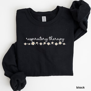 May include: Black sweatshirt with the text "respiratory therapy" in white cursive lettering and a row of white daisy flowers below the text.
