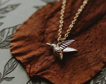 Alas elegantes. Un pequeño collar talismán de colibrí dorado de estilo bohemio.