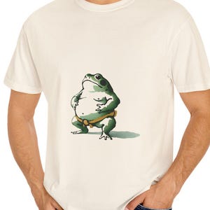 May include: A white t-shirt with a green frog wearing a yellow loincloth printed on the front.