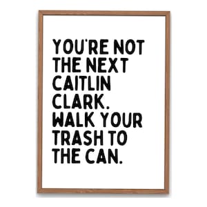 Pode incluir: Uma impressão de arte emoldurada com fundo branco e texto preto que diz: "YOU'RE NOT THE NEXT CAITLIN CLARK. WALK YOUR TRASH TO THE CAN." A moldura é de cor castanho claro.