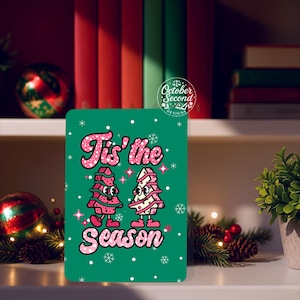 May include: A green Christmas card with the text "Tis' the Season" in pink, featuring two cartoon Christmas trees. The trees have pink and white details, and the card is decorated with snowflakes. The card is from October Second Designs.