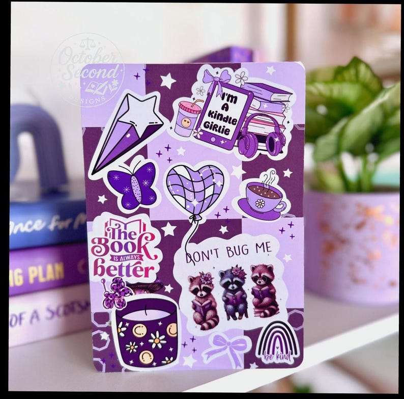 May include: A purple and white checkered notebook covered in stickers. Stickers include a star, butterfly, heart-shaped balloon, coffee cup, raccoons, and the text "I'm a Kindle Girlie" and "The Book is Always Better".
