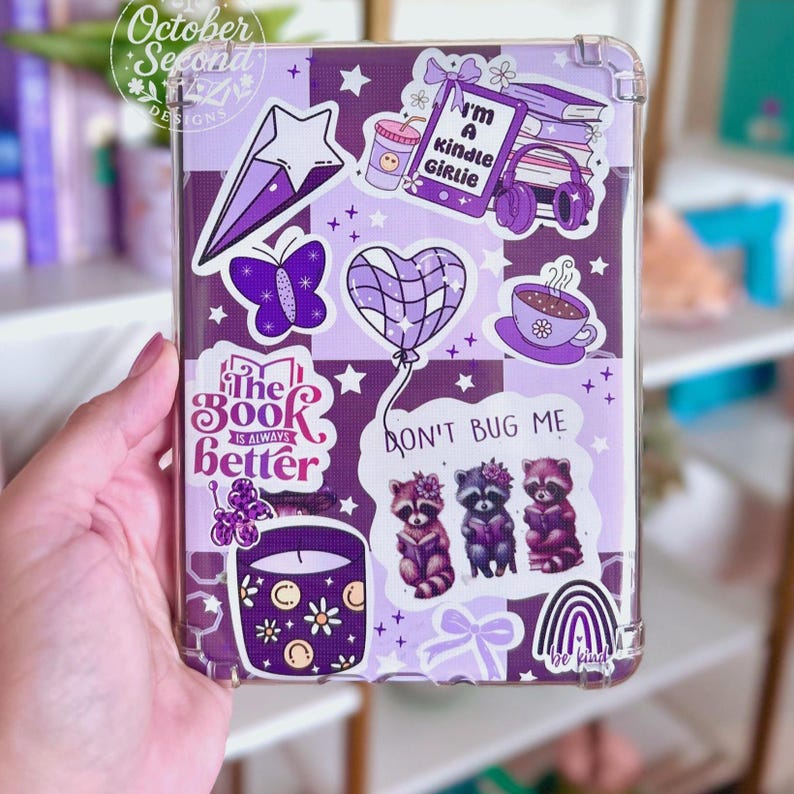 May include: Clear phone case with a purple and white checkered pattern, decorated with stickers. Stickers include a star, butterfly, heart balloon, raccoons, coffee cup, and the text "I'm a Kindle Girlie" and "The Book is Always Better."