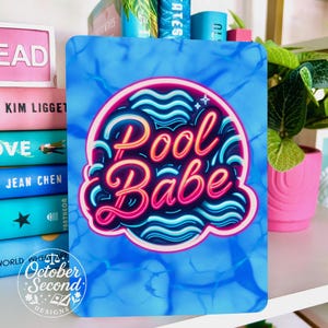 May include: A blue rectangular sign with the words "Pool Babe" in a neon-style design. The sign has a water-like background and is surrounded by books and a pink flower pot.