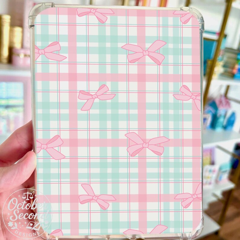 A hand is holding a clear case with a pink and green checkered pattern of bows on it.