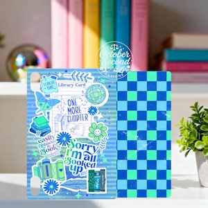 May include: A blue and green phone case with a book theme. The case features a striped design with book-related stickers, including a butterfly, globe, and the text "One More Chapter." The right side has a blue and green checkerboard pattern.