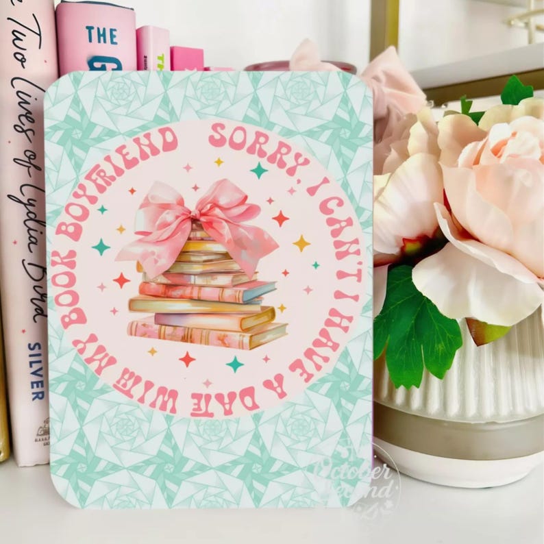 A colorful card with a bow and a stack of books, placed on a shelf next to a vase of flowers.