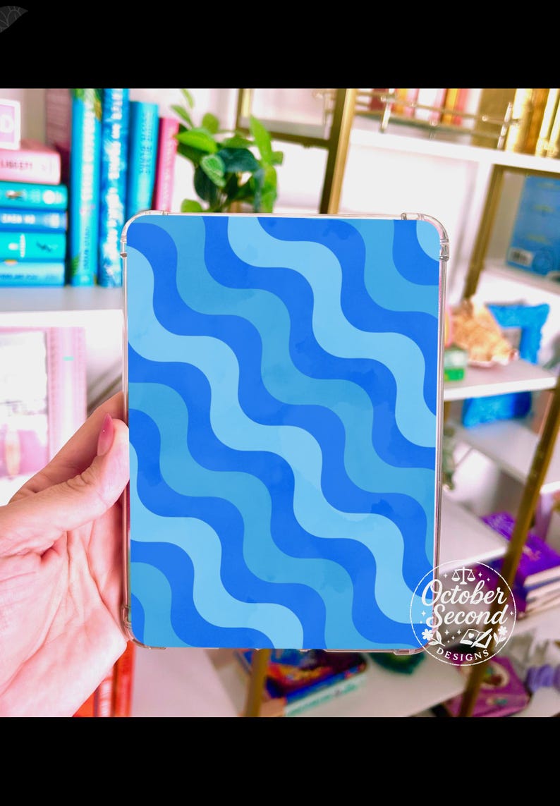 May include: A clear tablet case featuring a wavy pattern in shades of blue. The design is composed of alternating light and dark blue curved lines. The case has rounded corners and a logo that reads "October Second Designs."