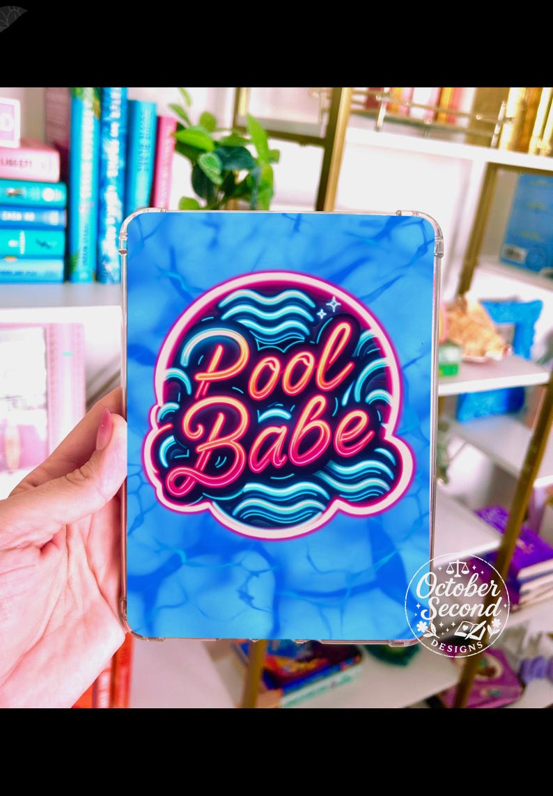 May include: A clear phone case featuring a blue water pattern background. The case has a neon pink and blue design that says "Pool Babe". The October Second Designs logo is in the bottom right corner.