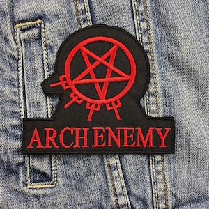 May include: A black patch featuring a red pentagram design and the word "ARCHENEMY" embroidered in red. The patch is rectangular with a unique shape, attached to a denim jacket.