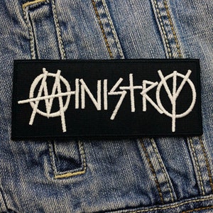 May include: A black rectangular patch with the word "MINISTRY" embroidered in white, featuring a stylized design. The patch is set against a denim background.