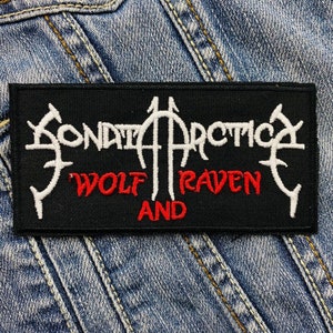 May include: A black rectangular patch with white and red embroidered text. The white text reads "SONATA ARCTICA" and the red text reads "WOLF RAVEN AND". The patch is set against a denim background.