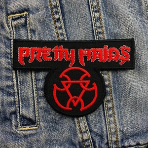 Op de afbeelding: Een zwart embleem met de tekst "PRETTY MAIDS" in rode, gestileerde letters. Daaronder een rond embleem met een rood, geometrisch ontwerp. De emblemen zijn op een spijkerjas genaaid.