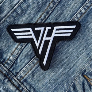 May include: Black and white embroidered patch featuring the iconic Van Halen logo. The patch is rectangular with a black background and white stitching, showcasing the band's distinctive emblem. The patch is set against a denim background.