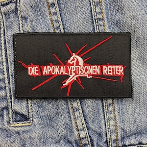 Può includere: Toppa rettangolare nera con testo e disegno ricamati in rosso e bianco. Il testo recita "DIE APOKALYPTISCHEN REITER" con una grafica di cavallo e cavaliere bianca. La toppa è su uno sfondo in denim.