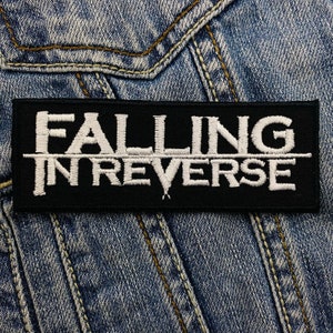May include: A black rectangular patch embroidered with the words "FALLING IN REVERSE" in white. The patch is set against a blue denim background, with visible stitching.