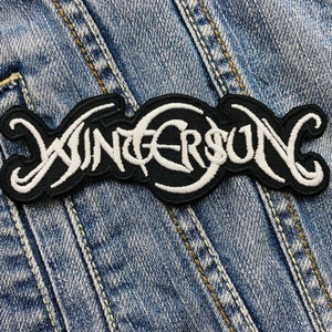 May include: Embroidered black and white patch featuring the word "WINTERSON" in a decorative font. The patch is set against a blue denim fabric, with visible stitching.