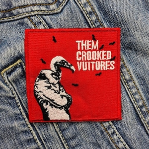 Op de afbeelding: Een vierkant, rood geborduurd embleem met de tekst "THEM CROOKED VULTURES" in het wit. Het embleem toont een zwart-wit illustratie van een gier en kleine zwarte vleermuis silhouetten.
