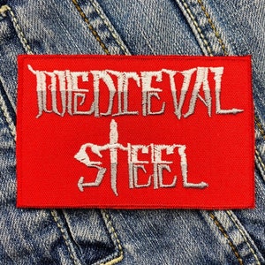 Peut inclure: Un écusson rectangulaire rouge avec les mots "MEDIEVAL STEEL" brodés en blanc. L'écusson est posé sur un fond en denim, mettant en valeur la texture du tissu.
