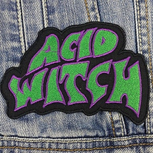 Puede incluir: Parche bordado negro con las palabras "ACID WITCH" en letras verdes con contorno morado. El parche está sobre un fondo de mezclilla azul.