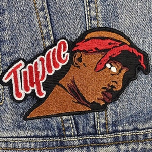 May include: Embroidered patch featuring a portrait of Tupac Shakur with a red bandana and the name "Tupac" in red script. The patch is on a denim background, showcasing the patch's details and colors.