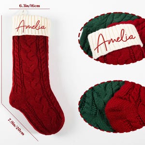 May include: A red cable-knit Christmas stocking with a cream-colored cuff. The stocking is 12.2 inches (31 cm) long and 7.9 inches (20 cm) wide. The name "Amelia" is embroidered on the cuff. The stocking is a festive holiday decoration.