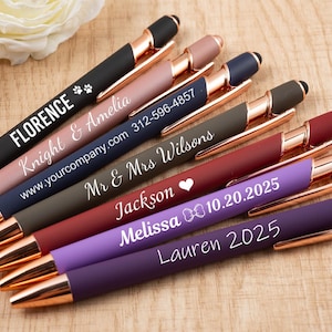 May include: A selection of personalised pens in shades like black, pink, navy, olive, burgundy, purple, and dark purple. The pens have gold-coloured details and custom text, including names, dates, and website addresses.