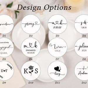 Pode incluir: Uma cole&ccedil;&atilde;o de doze etiquetas circulares brancas rotuladas de D1 a D12, cada uma apresentando texto preto e designs gr&aacute;ficos incluindo nomes, datas, cora&ccedil;&otilde;es, rosas e detalhes florais sob o t&iacute;tulo Design Options em fonte serifada.