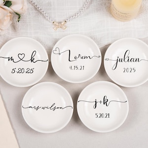 Pode incluir: Cinco pratos redondos de cer&acirc;mica branca com caligrafia preta personalizada. Os pratos exibem v&aacute;rios nomes, iniciais e datas, incluindo m&k 5.20.25, Lorem 4.15.21, julian 2025, mrs.wilson e j+k 5.20.21.