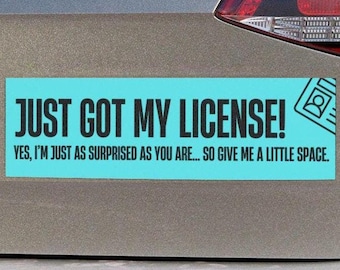 May include: A rectangular bumper sticker with the text "JUST GOT MY LICENSE!" in bold black letters on a light blue background. The text below reads "YES, I'M JUST AS SURPRISED AS YOU ARE... SO GIVE ME A LITTLE SPACE." A driver's license icon is on the right.