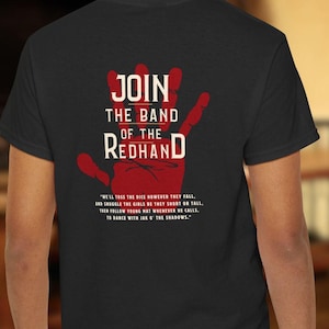 May include: Black t-shirt with a red handprint graphic and the text "JOIN THE BAND OF THE REDHAND". The text below the graphic reads "WE'LL TOSS THE DICE HOWEVER THEY FALL, AND SHUGGLE THE GIRLS BE THEY SHORT OR TALL. THEN FOLLOW YOUNG HAT WHENEVER HE CALLS, TO DANCE WITH JAK O' THE SHADOWS."