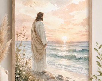 May include: A framed watercolor print depicting a figure with long hair wearing a white robe and a tan shawl, standing on a rocky shore looking out at a calm ocean during a soft pink and orange sunset with gentle waves and small birds in the sky.