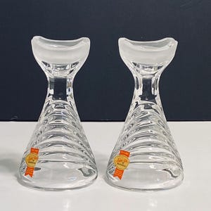 May include: Two clear glass candle holders with a textured, spiral design. Each holder has a small orange label with the word "remarkable" printed on it.